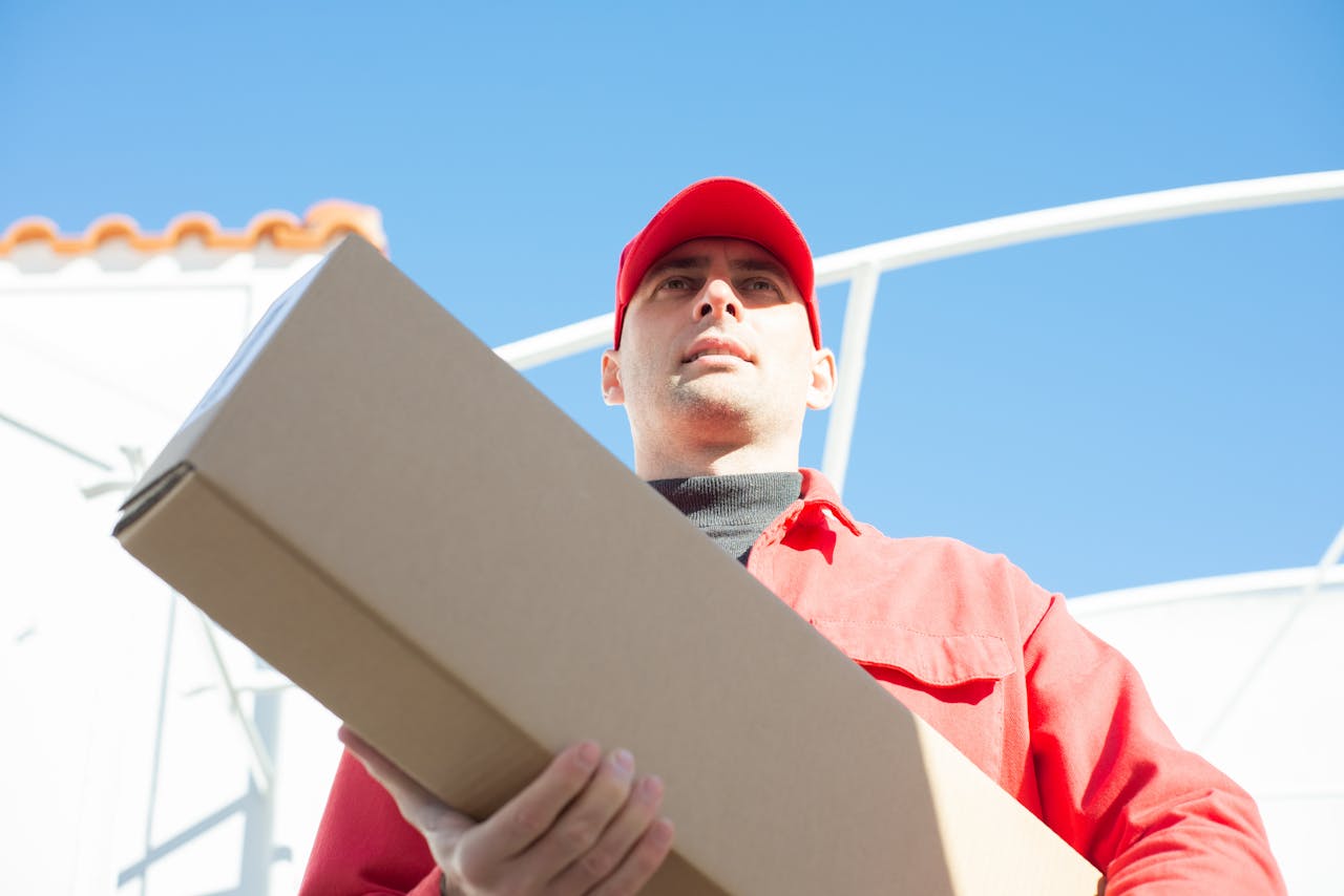 services-03 Delivery person in red uniform holding a parcel, captured with a low angle against a clear sky.